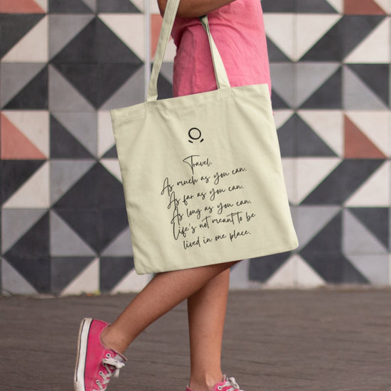 A person in a pink shirt and sneakers walks with the Horizon Seeker Tote Bag, an eco-friendly, cream-colored bag displaying a quote in black cursive. The background features gray and white geometric tiles.