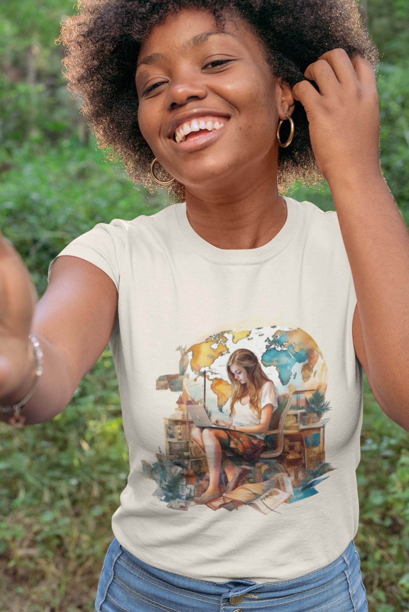 A smiling woman with curly hair takes a selfie outdoors, epitomizing the spirit of a digital nomad. She wears the Wanderlust Workspace Tee, which displays a graphic of a woman using a laptop amid a watercolor-style world map and numerous plants. The vibrant green backdrop complements her wanderlust-inspired setting.