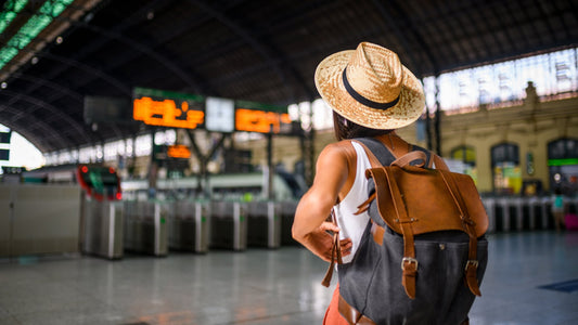 Woman traveler with straw hat and backpack looking at departure board in train station, ready for adventure